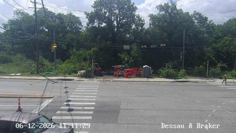 Construction workers and equipment are present on the roadside.