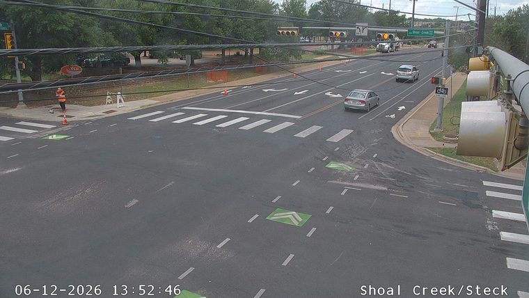 Person in high-visibility vest and orange cones present at intersection.