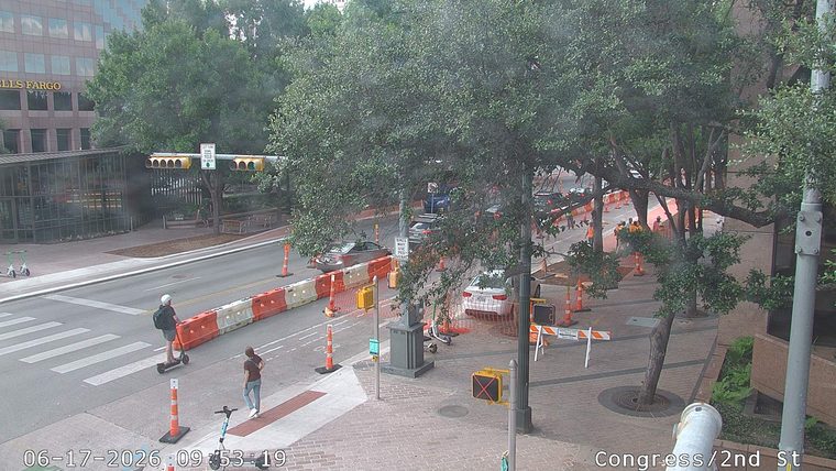 Construction workers in orange vests are present on the roadway.