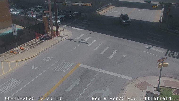 Debris and orange cones are present on the side of the road near a construction barrier.