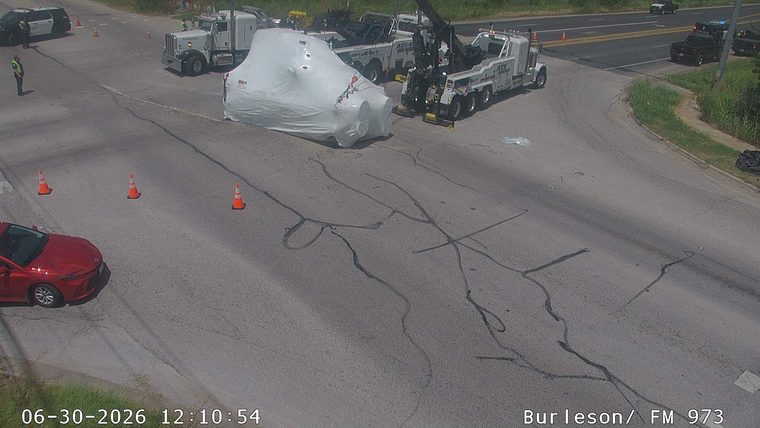 Police car and tow trucks attending to a large object covered in white tarp in the intersection