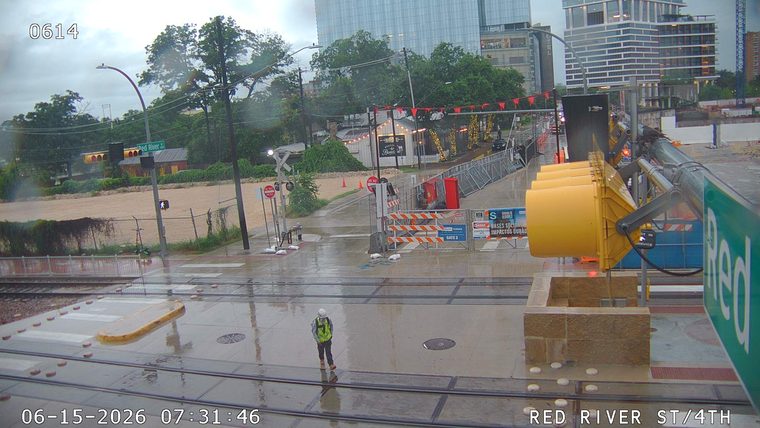 Worker in reflective vest and hard hat stands on wet ground near construction barriers.