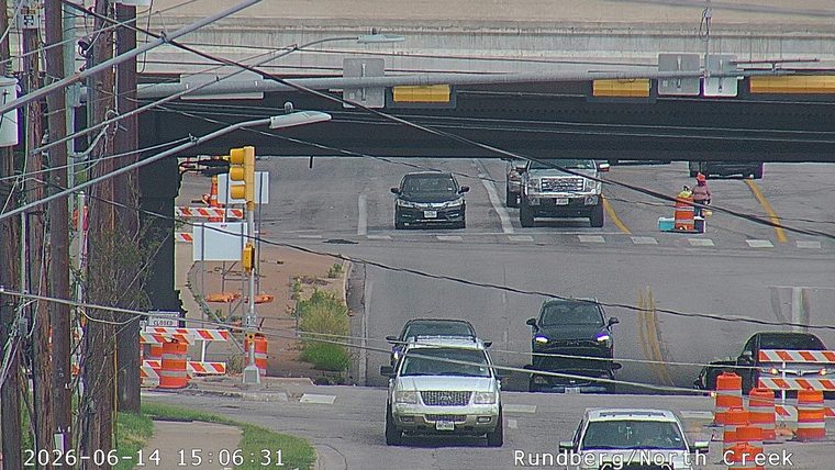 Person in orange vest near traffic cones and equipment on roadway.
