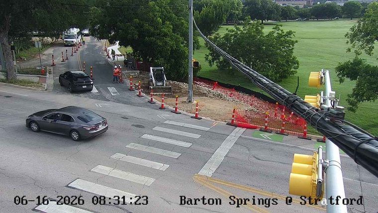 Construction workers and equipment present on the roadway, traffic cones visible.