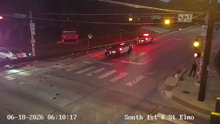 Two police cars with lights on at an intersection with people on the sidewalk.