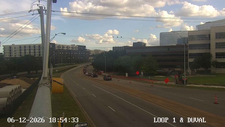 Construction zone with cones, barriers, and a small excavator on the side of the road.
