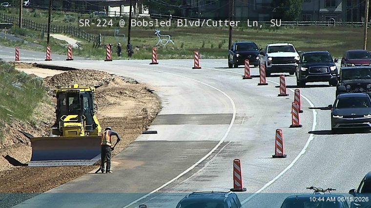 Road construction with a bulldozer and worker present, traffic cones redirecting vehicles.