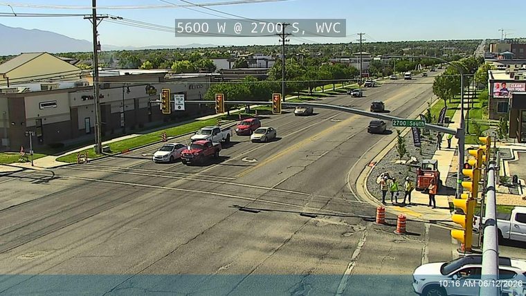 Construction workers and equipment are present at the intersection, indicating road work.