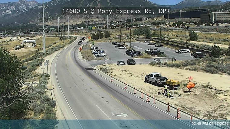 Two workers and equipment are on the roadside, with traffic cones and a sign.