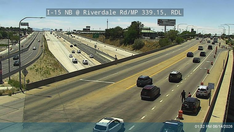 Police officer and two civilians near stopped vehicles on the right shoulder.