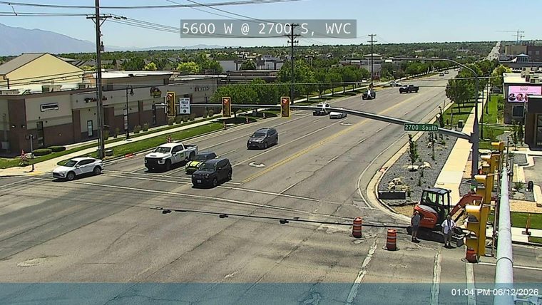 Construction workers and equipment are present at the intersection, with traffic cones visible.