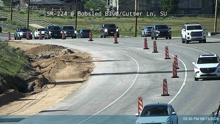 Roadway partially blocked by dirt and debris from embankment erosion, with traffic cones present.