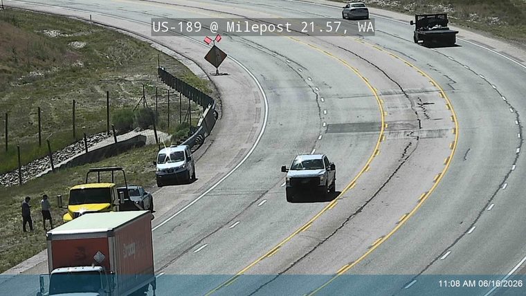 Tow truck and two people on the shoulder near a disabled vehicle.