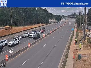 Two workers in high-visibility vests are present near construction on the roadside.