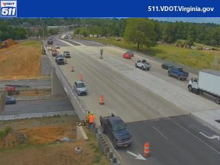 Construction workers and equipment on the roadway indicate ongoing work.