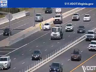Person in yellow vest on highway shoulder near traffic.