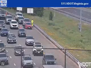 Responder in yellow vest on shoulder near stopped traffic.