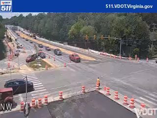 Construction worker directing traffic near a crosswalk with orange cones and barriers.