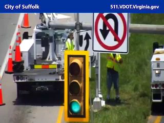 Two workers in safety vests near a truck and traffic signal.