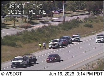 Two people in safety vests stand near stopped vehicles on the shoulder.