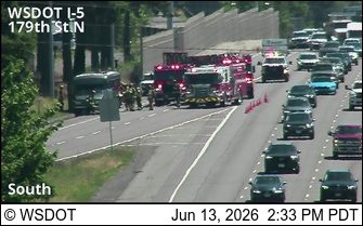 Multiple fire trucks and emergency personnel on the highway shoulder.