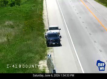 Police vehicle and tow truck on the shoulder, traffic moving normally.