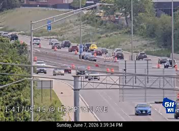 Emergency responders and traffic cones are present on the roadway, indicating an incident.