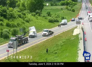 Tow truck and other vehicles stopped on the highway shoulder with personnel present.