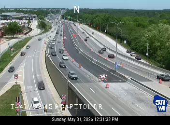 Emergency responders and equipment on the highway shoulder with cones.