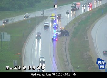 Multiple vehicles involved in a crash on a wet highway with emergency lights visible.