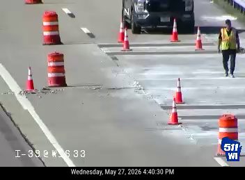 Worker in safety vest near cones and construction on roadway.
