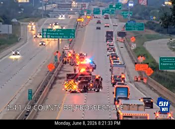 Emergency responders with flashing lights on the highway shoulder near traffic.