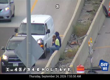 Two persons sitting on the concrete barrier next to a white van on the right shoulder