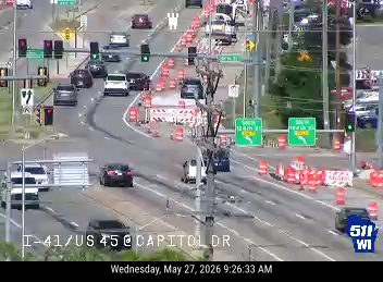 Orange construction barrels and barriers are present on the roadway, indicating a possible incident or road work.