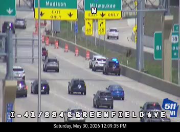 Police car with lights on, traffic cones, and stopped vehicles indicate a possible incident.