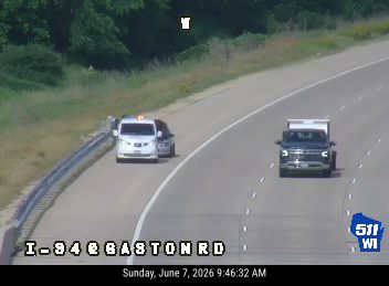 Two white vans and a dark truck are stopped on the shoulder of the highway.