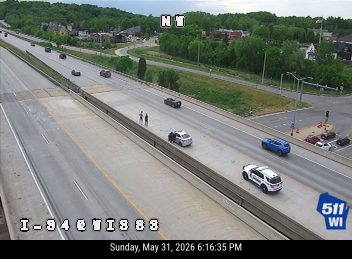 Two police vehicles and two individuals on the shoulder of the highway.