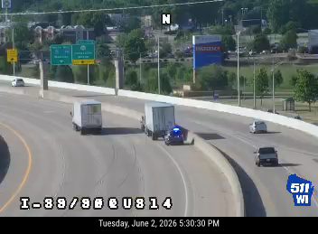 Police car and trucks stopped on highway shoulder, possibly responding to an incident.