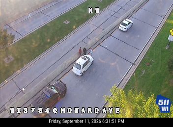 Police car with lights on the shoulder next to a white vehicle with people standing outside