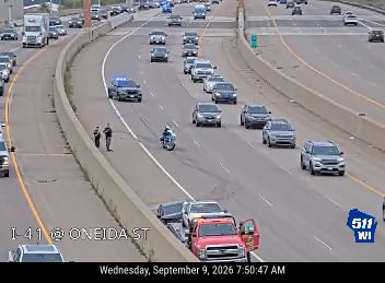 Two police cars and a motorcycle officer with lights on in the left lane