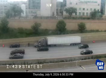 Tractor-trailer and two cars in the roadway, with cones and a person visible
