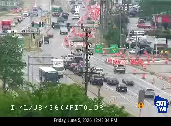 Emergency responders and traffic cones are present on the roadway, indicating an incident.