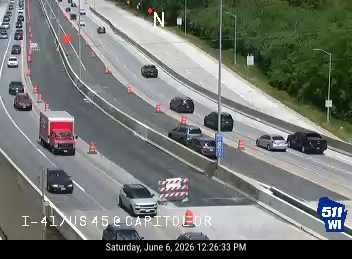 Emergency vehicles and cones on the highway indicate an incident response.