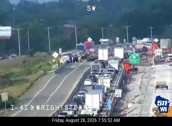 Multiple vehicles in lanes with construction cones and workers present
