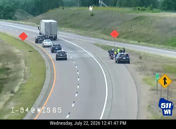 Motorcycle and two vehicles on the right shoulder with orange cones and workers