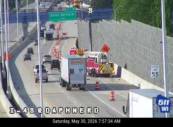 Police and emergency vehicles on the highway shoulder with cones and flashing lights.