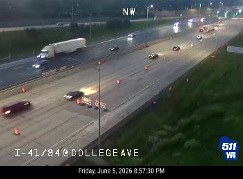 Two vehicles appear to be involved in a crash on the highway, with cones and barriers present.