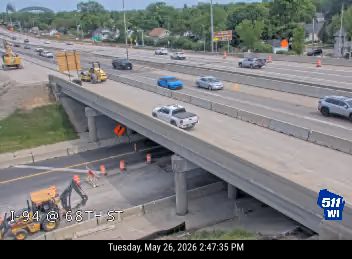 Construction workers and equipment are present on the roadway, indicating ongoing work.
