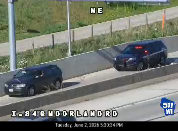 Two police vehicles with lights on are stopped on the shoulder of the highway.