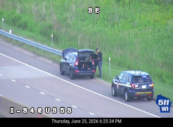 Police car with lights on the shoulder next to a vehicle with an open trunk